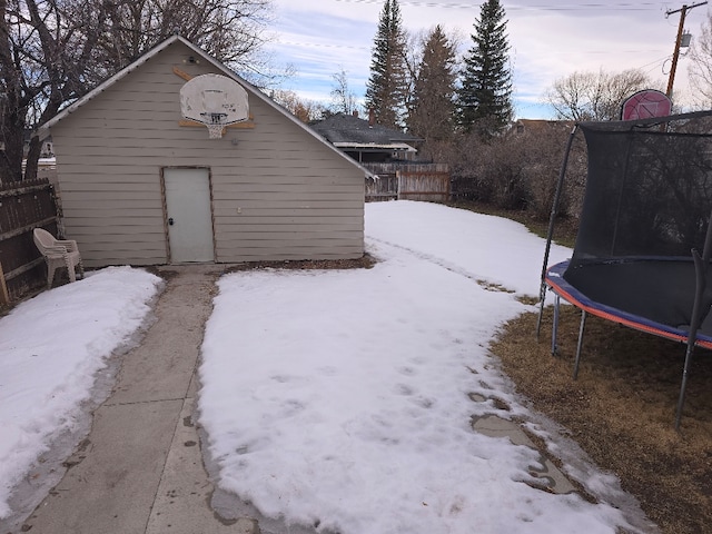 snow covered structure with a trampoline, an outdoor structure, and fence