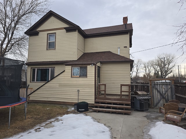 snow covered back of property featuring a patio, a chimney, a trampoline, fence, and a deck