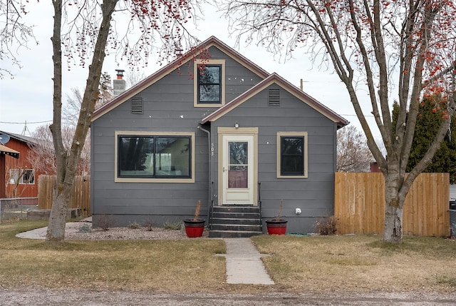 bungalow with entry steps, a front lawn, a chimney, and fence