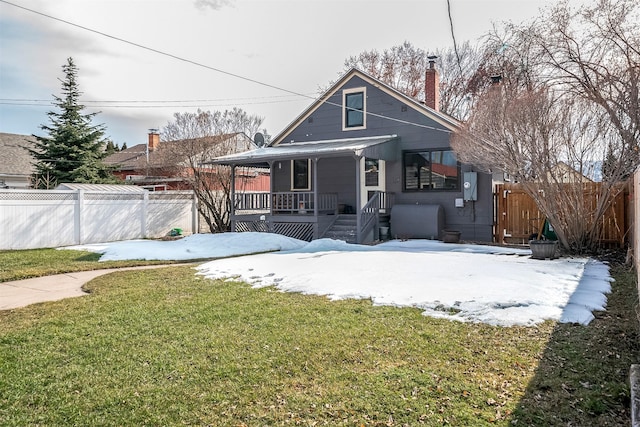 snow covered back of property with covered porch, a yard, and fence private yard