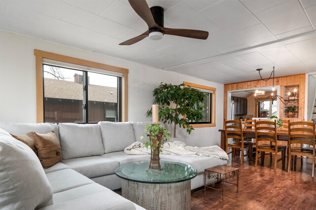 living area featuring dark wood-style flooring, wooden walls, and ceiling fan with notable chandelier