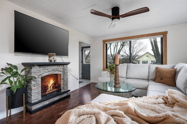 living area featuring wood finished floors, a stone fireplace, a ceiling fan, and a healthy amount of sunlight