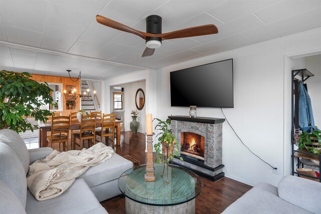 living room featuring stairway, a stone fireplace, wood finished floors, and ceiling fan with notable chandelier