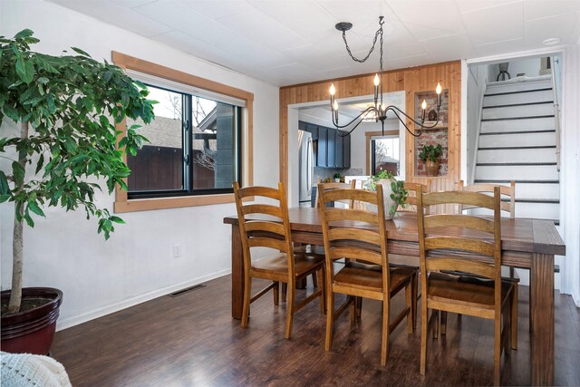 dining space featuring dark wood finished floors, wooden walls, visible vents, a chandelier, and stairs