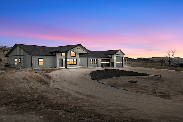 modern farmhouse featuring a shingled roof, an attached garage, board and batten siding, fence, and driveway