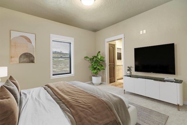 bedroom with light carpet, baseboards, a textured ceiling, and ensuite bathroom