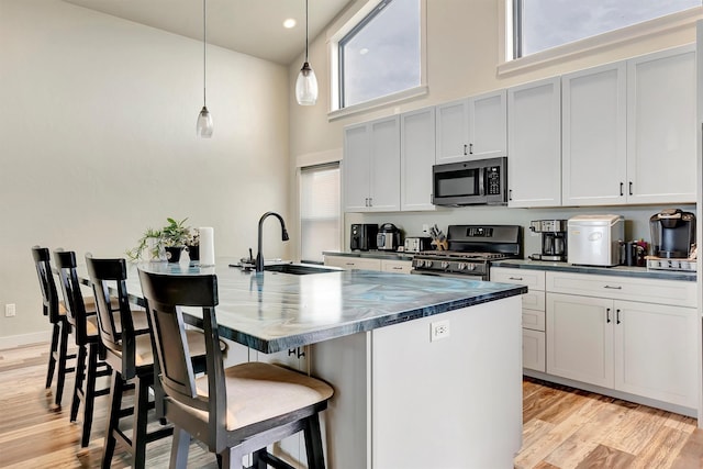 kitchen with dark countertops, appliances with stainless steel finishes, a high ceiling, a kitchen bar, and a sink