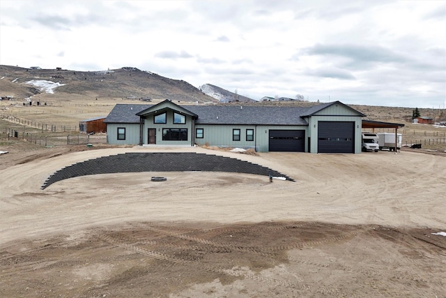 view of front of home with driveway, roof with shingles, an attached garage, fence, and a mountain view