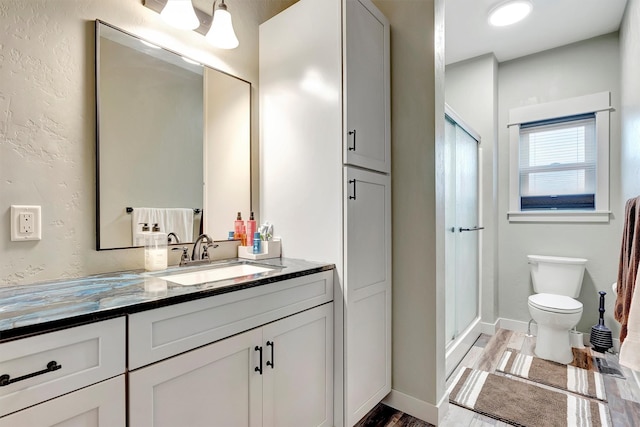 bathroom with a stall shower, baseboards, toilet, wood finished floors, and vanity