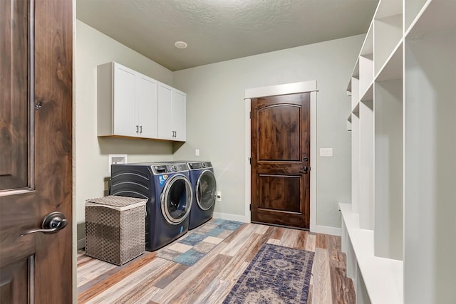 laundry room with washer and clothes dryer, cabinet space, light wood-style flooring, a textured ceiling, and baseboards