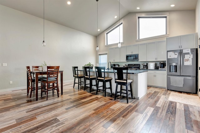 kitchen featuring a center island with sink, dark countertops, appliances with stainless steel finishes, light wood-style floors, and a kitchen breakfast bar