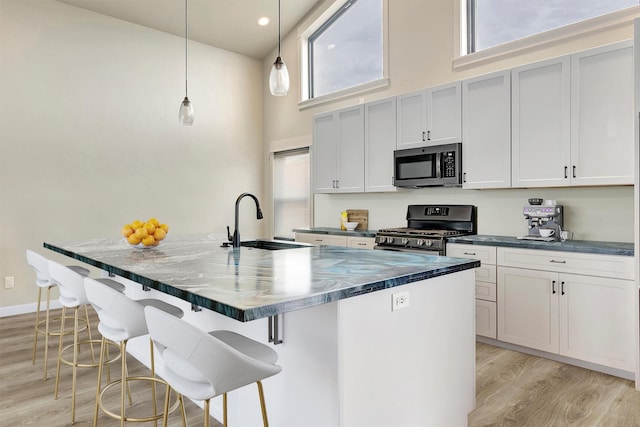 kitchen with dark countertops, gas range, stainless steel microwave, a high ceiling, and a sink