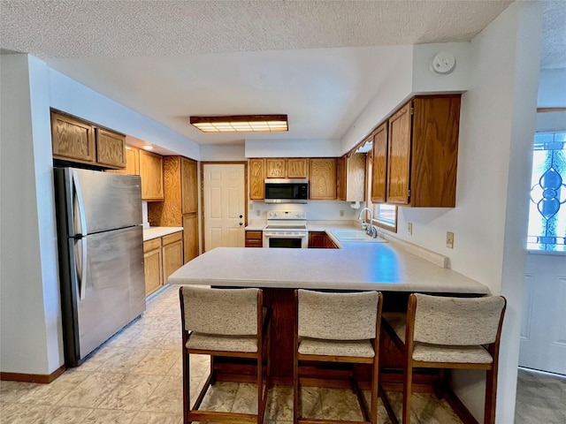 kitchen featuring a peninsula, brown cabinetry, appliances with stainless steel finishes, and light countertops