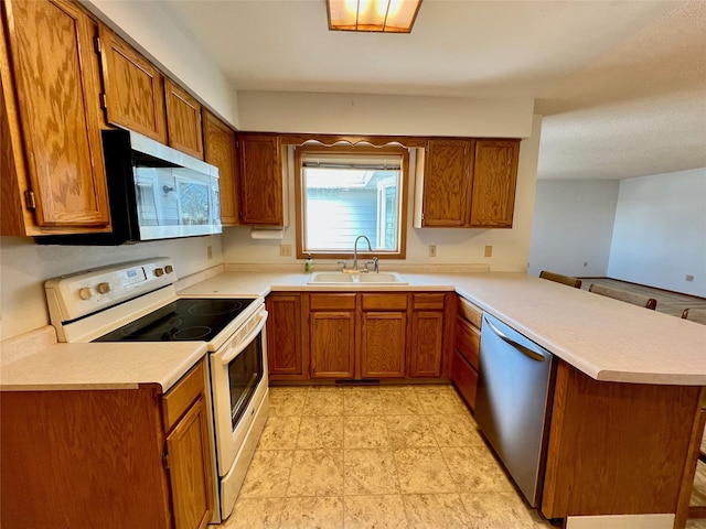 kitchen featuring stainless steel appliances, brown cabinetry, a sink, and a peninsula