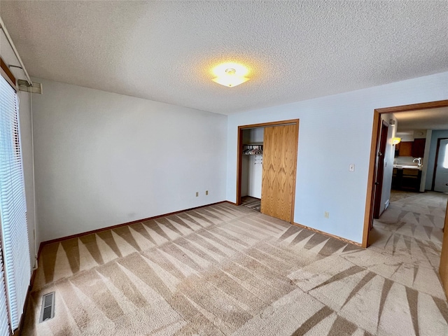 unfurnished bedroom featuring a closet, visible vents, light carpet, a textured ceiling, and baseboards