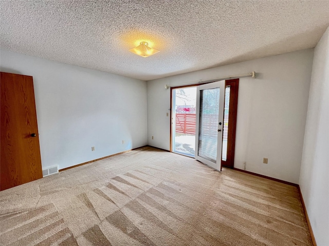 carpeted empty room featuring visible vents, a textured ceiling, and baseboards