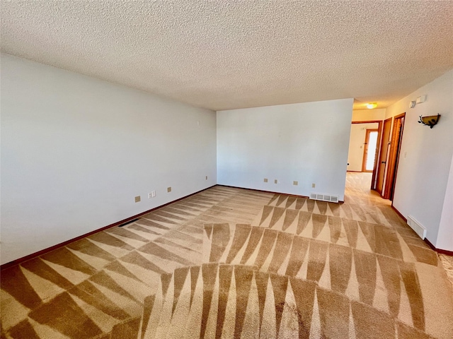 carpeted empty room featuring a textured ceiling, visible vents, and baseboards