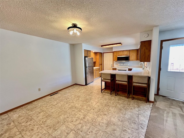 kitchen featuring brown cabinets, stainless steel appliances, light countertops, a sink, and a peninsula