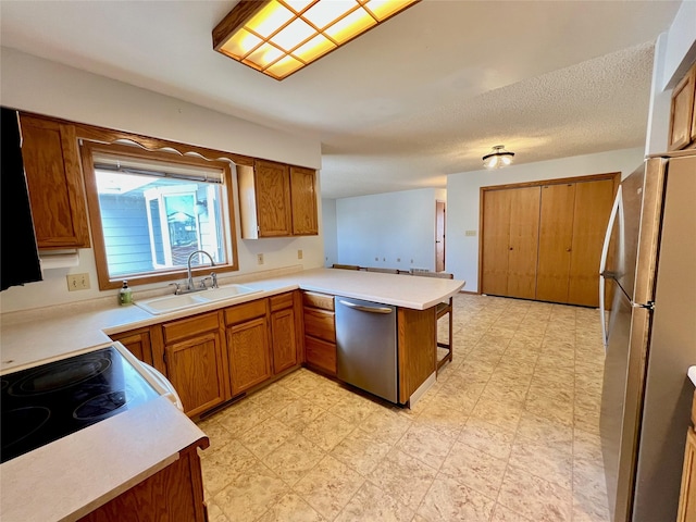 kitchen featuring appliances with stainless steel finishes, brown cabinets, a peninsula, light floors, and a sink