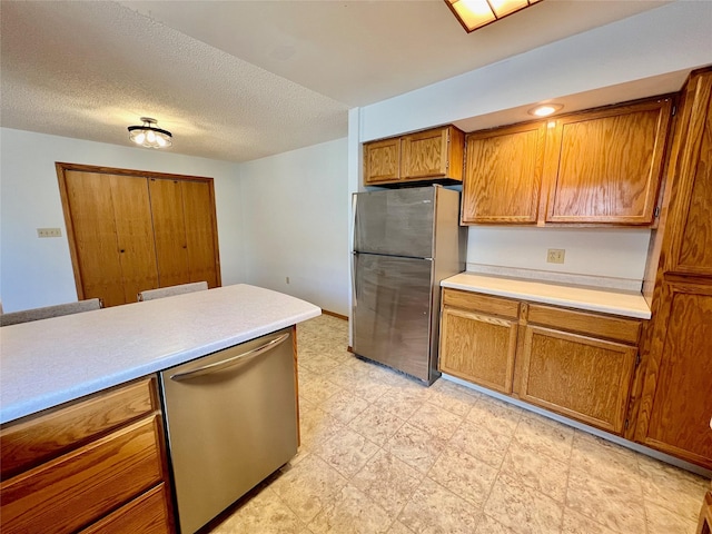 kitchen featuring a textured ceiling, stainless steel appliances, light countertops, light floors, and brown cabinetry