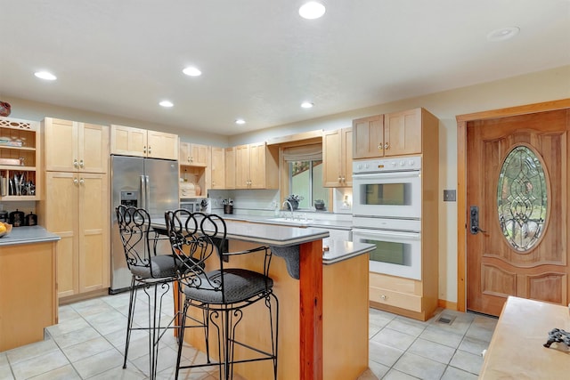 kitchen featuring white double oven, a breakfast bar area, light brown cabinets, recessed lighting, and stainless steel fridge