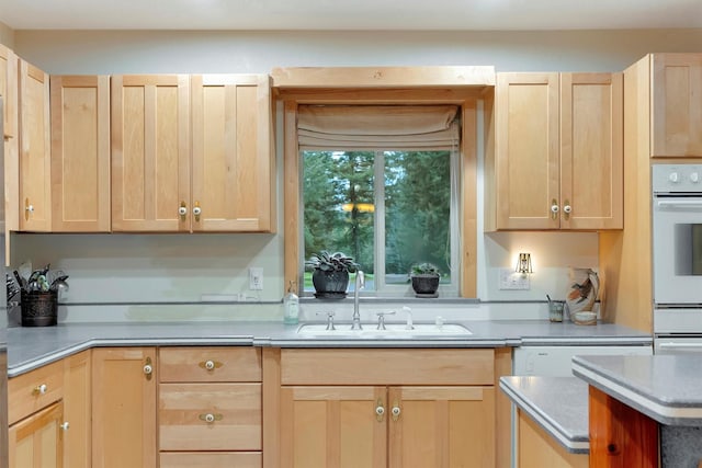 kitchen with white double oven, light countertops, a sink, and light brown cabinetry