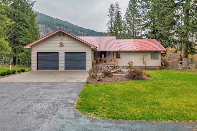 single story home with metal roof, a porch, a garage, concrete driveway, and a front lawn