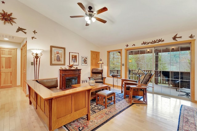 living room featuring lofted ceiling, light wood-style flooring, visible vents, and a glass covered fireplace