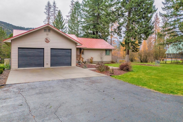 ranch-style home with driveway, metal roof, an attached garage, and a front lawn