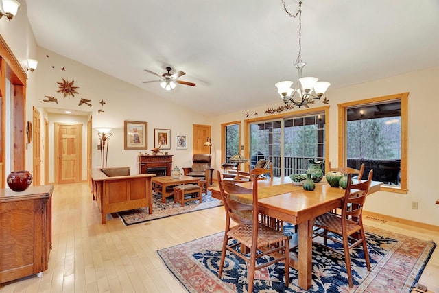 dining area featuring lofted ceiling, light wood-style flooring, a fireplace, and ceiling fan with notable chandelier