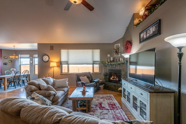 living area with lofted ceiling, a glass covered fireplace, wood finished floors, and a ceiling fan