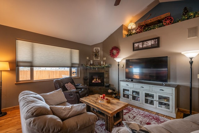 living room featuring lofted ceiling, wood finished floors, visible vents, baseboards, and a tiled fireplace