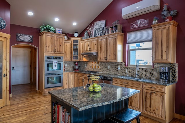 kitchen with arched walkways, appliances with stainless steel finishes, an AC wall unit, under cabinet range hood, and a sink