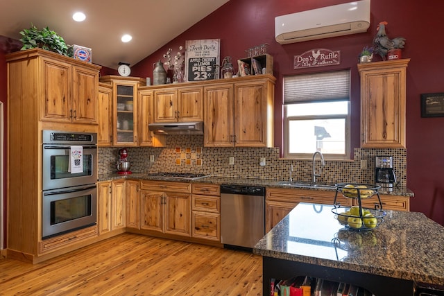 kitchen with lofted ceiling, under cabinet range hood, a sink, an AC wall unit, and appliances with stainless steel finishes