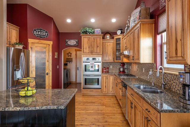 kitchen with arched walkways, stainless steel appliances, light wood-style flooring, separate washer and dryer, and under cabinet range hood