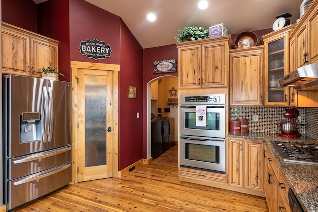 kitchen featuring appliances with stainless steel finishes, vaulted ceiling, light wood-type flooring, under cabinet range hood, and backsplash