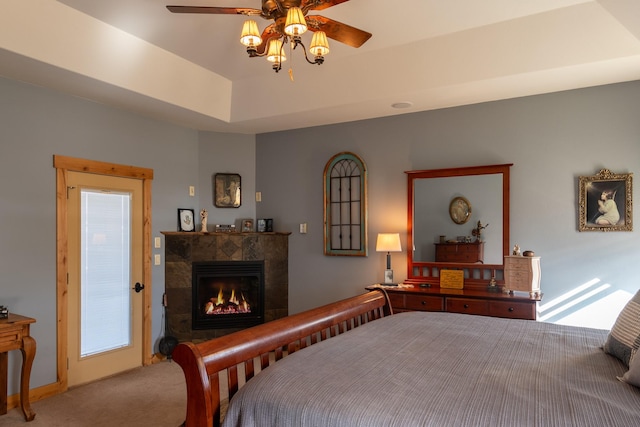 carpeted bedroom with a tile fireplace, a raised ceiling, and ceiling fan