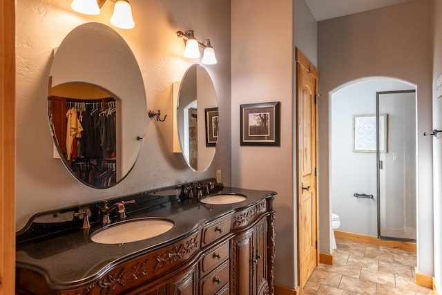 full bath featuring double vanity, a sink, toilet, and baseboards