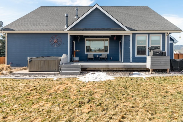 back of property with a hot tub, a shingled roof, and a lawn