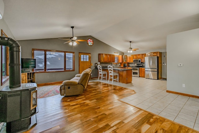 living room with a wood stove, light wood-style flooring, a ceiling fan, and lofted ceiling