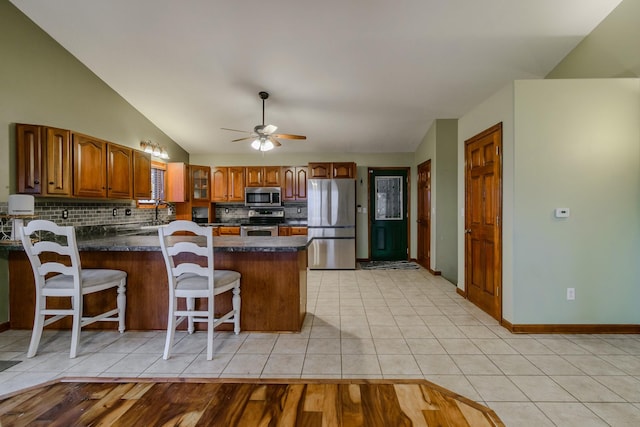 kitchen featuring stainless steel appliances, dark countertops, a peninsula, and light tile patterned floors