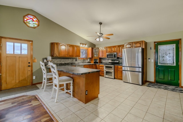 kitchen with light tile patterned floors, brown cabinetry, dark countertops, appliances with stainless steel finishes, and a peninsula