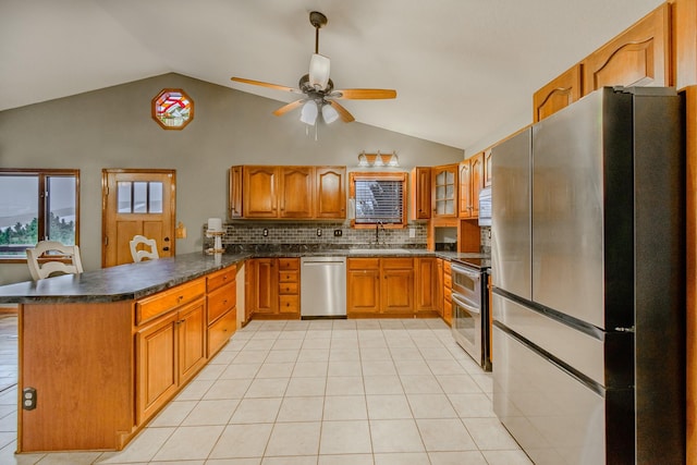 kitchen with brown cabinets, dark countertops, appliances with stainless steel finishes, a sink, and a peninsula