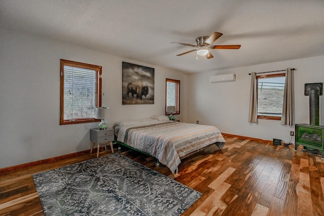 bedroom featuring a wall unit AC, baseboards, and wood finished floors