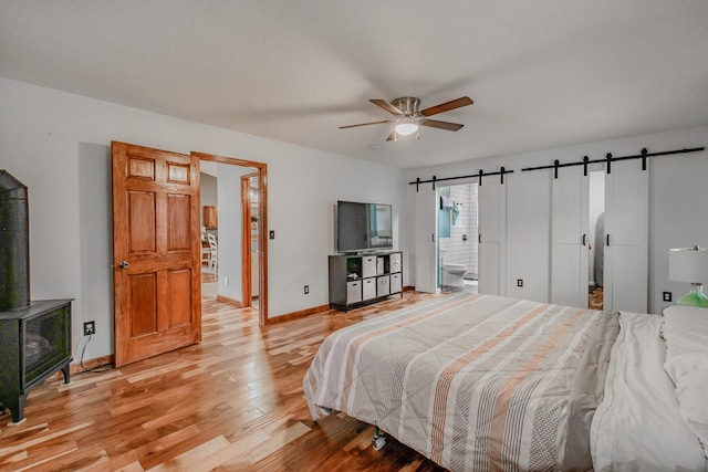 bedroom featuring a barn door, baseboards, ensuite bath, ceiling fan, and light wood-style flooring