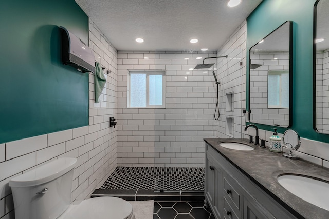 bathroom featuring tiled shower, toilet, a sink, a textured ceiling, and tile walls