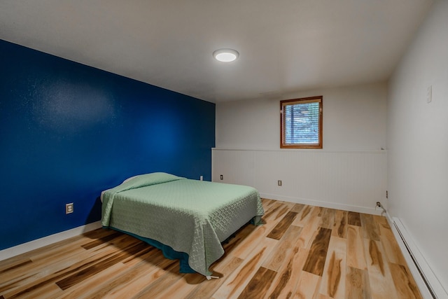 bedroom with baseboards, wainscoting, baseboard heating, and wood finished floors