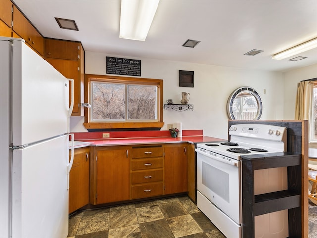 kitchen featuring white appliances, stone finish floor, visible vents, and brown cabinets