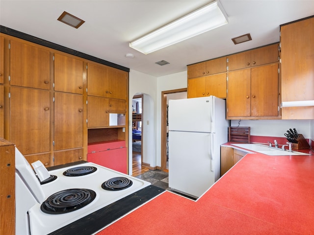 kitchen with brown cabinetry, arched walkways, white appliances, and visible vents