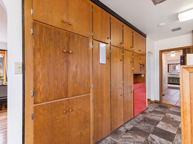 hallway with arched walkways, a baseboard radiator, visible vents, and baseboards